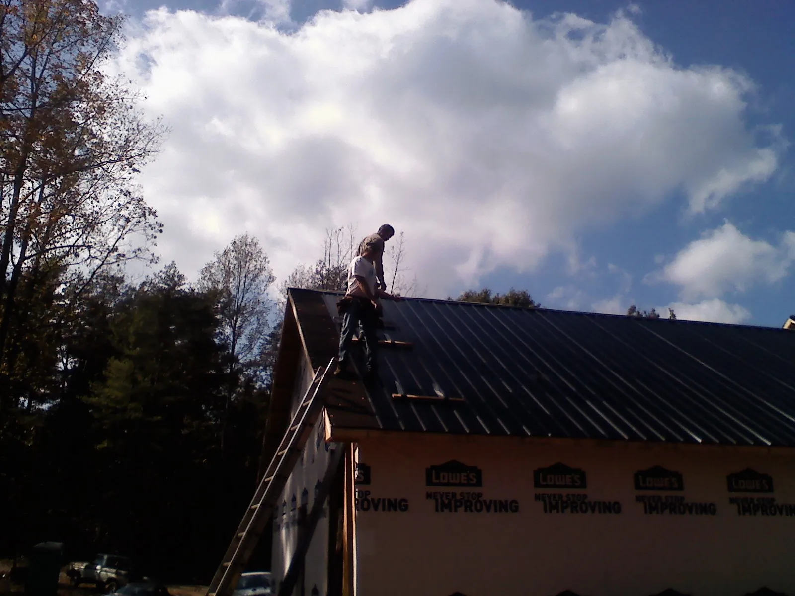 Roofer fastening dark metal panels high against a cloudy sky, from a Roof Inspection job in Millersville