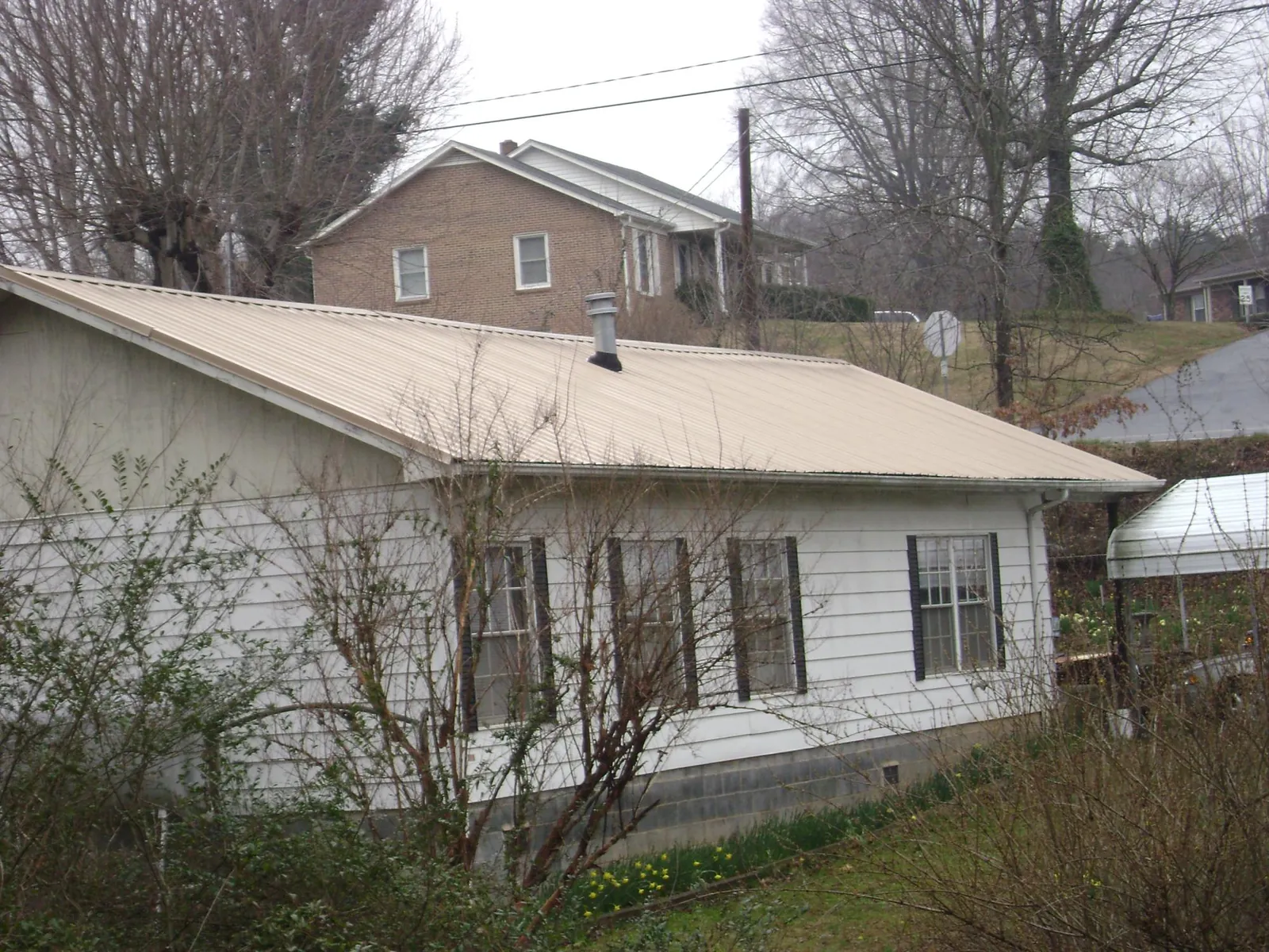 Tan metal roof on a white sided house set into a hillside — Commercial Roofing by Roofing Brothers in Millersville